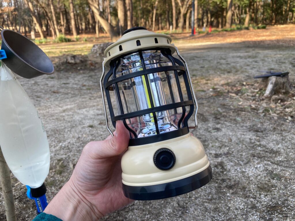 筆者がダイソーの調光機能付ランタンを手に持っています。