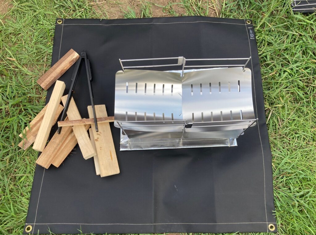 焚き火専用シート95×95㎝に薪や火ばさみを置いたもの